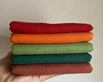 以下が含まれることがあります： 赤、オレンジ、緑、茶色の異なる色合いの生地見本が5つあります。見本は互いに積み重ねられています。