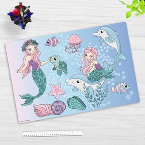 Puede incluir: Una sirena azul y rosa con el pelo largo rosa montando un delfín con una cola de sirena rosa y verde. El fondo es azul con burbujas blancas y otras criaturas marinas como una tortuga, una estrella de mar y un pez.