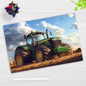 Könnte beinhalten: Ein grüner und schwarzer John Deere Traktor mit einem Fahrer in der Kabine, der durch ein Feld mit Heuballen unter einem blauen Himmel mit weißen Wolken fährt.