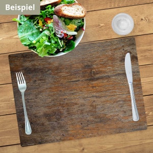 May include: A brown wooden placemat with a fork and knife on it. The placemat has a rustic, distressed look. The word "Beispiel" is written in white on a green background in the top left corner of the image.