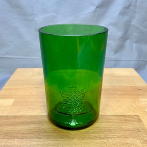 May include: A green glass tumbler with a decorative tree design etched near the base. The glass is cylindrical with a slightly rounded rim. The glass is made of a transparent green material.