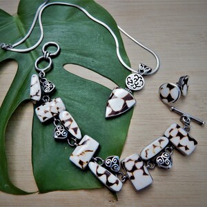 May include: A silver chain necklace with a pendant and a matching pair of earrings. The pendant and earrings are made of white and brown shell pieces.