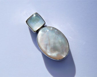 May include: A white oval and square shaped mother of pearl pendant with silver trim.