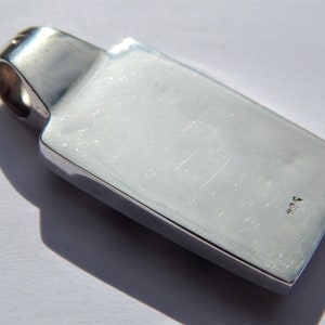 May include: Silver pendant with a rectangular shape and a smooth, polished surface. The pendant has a small loop at the top for attaching a chain. The back of the pendant is marked with the number "925".