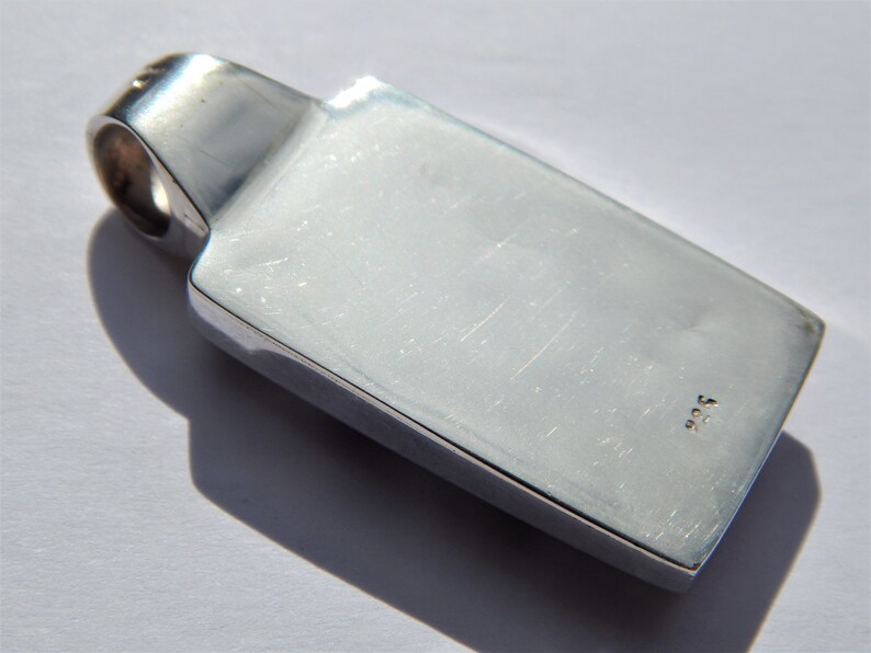 May include: Silver pendant with a rectangular shape and a smooth, polished surface. The pendant has a small loop at the top for attaching a chain. The back of the pendant is marked with the number "925".