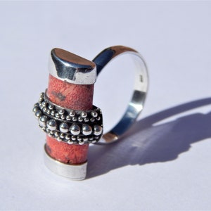 Puede incluir: Un anillo de plata con una piedra de coral rojo engastada en una banda de plata. La banda est&aacute; decorada con una fila de cuentas de plata.
