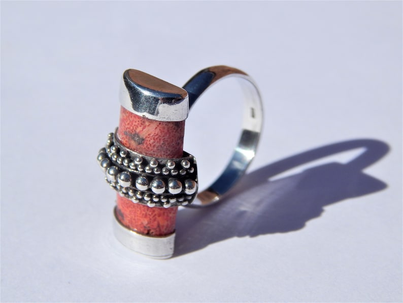Puede incluir: Un anillo de plata con una piedra de coral rojo engastada en una banda de plata. La banda est&aacute; decorada con una fila de cuentas de plata.