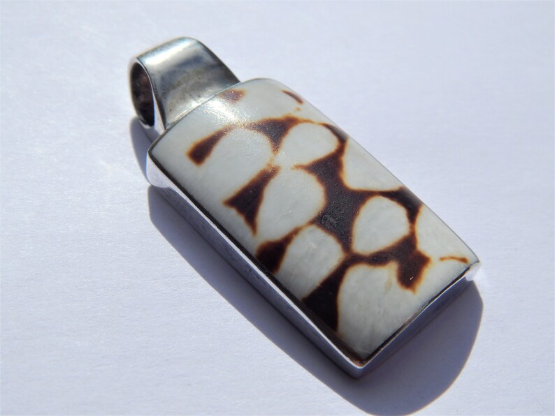 May include: A silver pendant with a rectangular white shell inlay featuring a brown and white pattern.