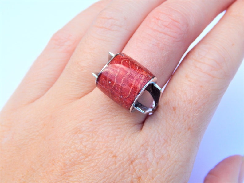 Puede incluir: Un anillo de plata con una piedra de coral rojo rectangular. El anillo tiene un dise&ntilde;o &uacute;nico con dos puntas en la parte superior y dos puntas en la parte inferior.
