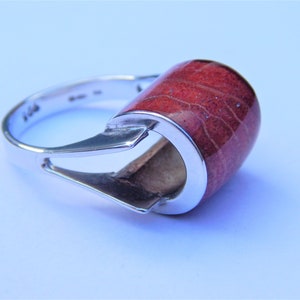 Puede incluir: Un anillo de plata con una piedra de coral rojo engastada en un dise&ntilde;o moderno y &uacute;nico.