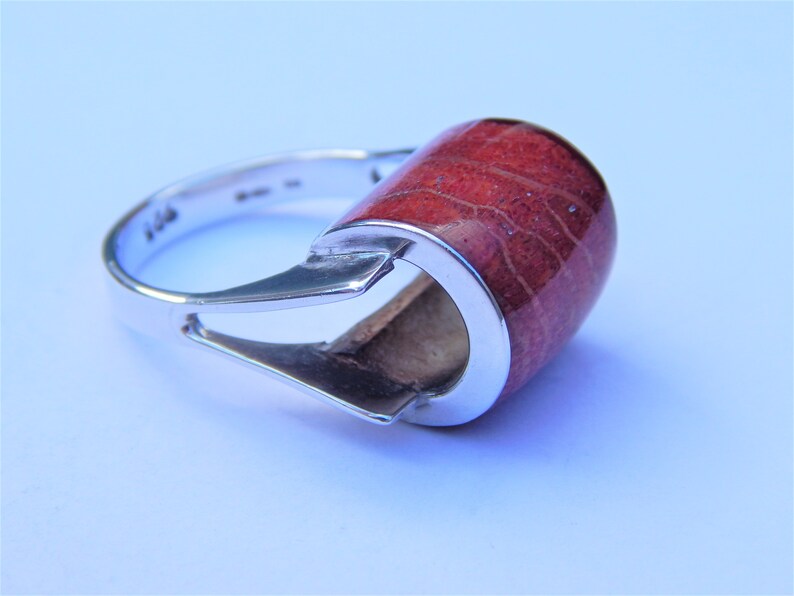 Puede incluir: Un anillo de plata con una piedra de coral rojo engastada en un dise&ntilde;o moderno y &uacute;nico.