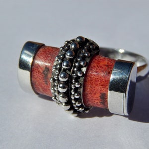 Puede incluir: Un anillo de plata con una piedra de coral rojo engastada en una banda de cuentas de plata.