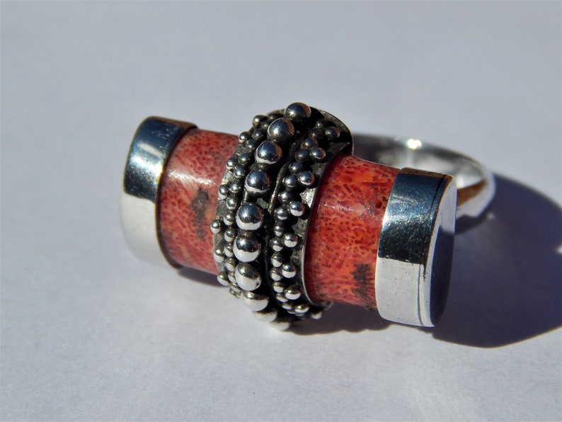 Puede incluir: Un anillo de plata con una piedra de coral rojo engastada en una banda de cuentas de plata.