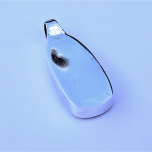 May include: A silver pendant with a smooth, oval shape. The pendant has a loop at the top for attaching a chain.