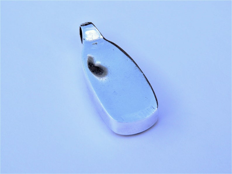 May include: A silver pendant with a smooth, oval shape. The pendant has a loop at the top for attaching a chain.