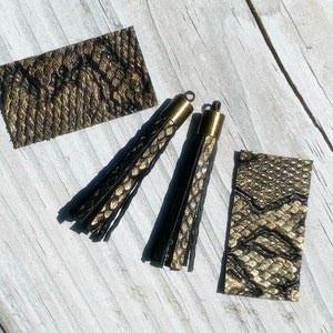 May include: Two black and gold tassel earrings with gold metal caps. The tassels are made of faux snakeskin fabric. There are two additional pieces of faux snakeskin fabric.