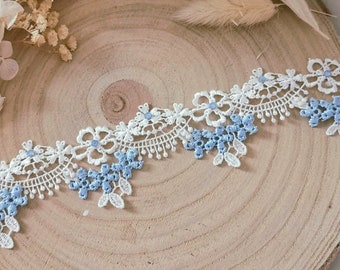 May include: White and blue lace trim with a floral design. The lace is delicate and intricate, with small flowers and leaves.