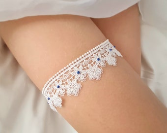May include: White lace garter with blue bead embellishments. The garter is delicate and features a floral design.