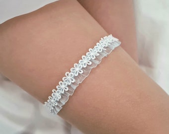 May include: White lace garter with a delicate floral design. The garter is made of soft, sheer fabric and has a ruffled edge.