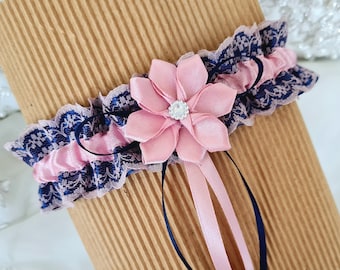 May include: A delicate blue and pink lace garter with a pink satin flower and a rhinestone embellishment. The garter has a blue satin ribbon.