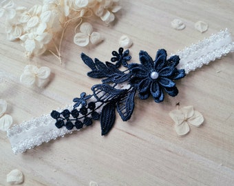 May include: A white lace garter with a navy blue floral applique and a pearl accent.