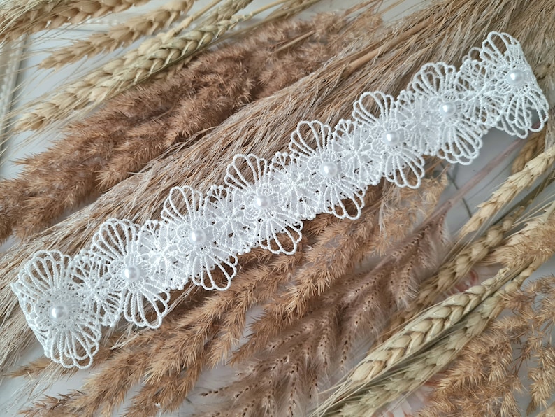 Op de afbeelding: Witte kant met parel accenten. De kant heeft een delicaat bloemenpatroon en is perfect om een ​​toets van elegantie toe te voegen aan elk project.