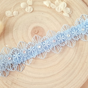 Op de afbeelding: Een lichtblauwe kanten kousenband met kleine strass steentjes. De kousenband ligt op een houten oppervlak.