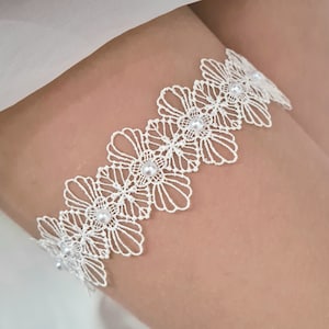 Op de afbeelding: Wit kanten kousenband met parelversiering. Het kousenband is gemaakt van delicate witte kant en heeft een rij parels.
