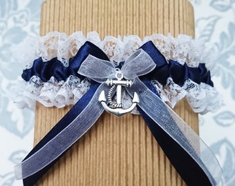 May include: A white lace garter with a navy blue satin ribbon and a silver anchor charm. The garter is tied with a white sheer ribbon.
