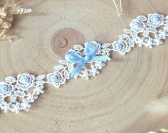 May include: Delicate white lace trim with a floral design, accented with small blue beads and a light blue satin bow. This decorative trim is perfect for bridal or craft projects.