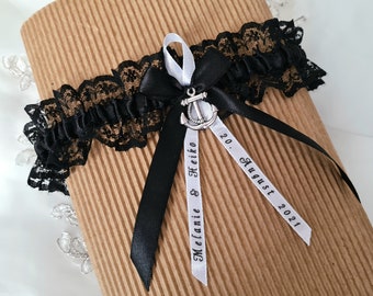 May include: Black and white bridal garter with a silver anchor charm and two white satin ribbons with the text "Melanie & Heiko" and "20. August 2021".