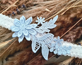 May include: A light blue lace garter with white lace trim and floral designs. The garter is on a brown background.
