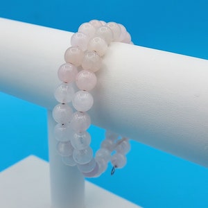 May include: A double-strand bracelet made of pink and white gemstone beads. The bracelet is on a white display stand.
