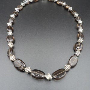 May include: A brown smoky quartz gemstone necklace with silver accents. The necklace is made of oval-shaped beads and has a silver clasp.