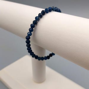 May include: A blue gemstone beaded bracelet on a white display stand. The bracelet is made of small, faceted beads.