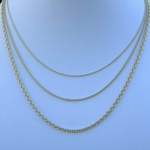 May include: Four gold chains of different lengths and thicknesses, layered on a white mannequin bust.