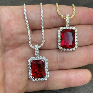 Peut inclure: Deux chaînes en argent et en or avec des pendentifs en pierre rouge. Les pendentifs sont de forme carrée avec une auréole de petites pierres blanches autour de la pierre rouge.