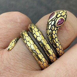 May include: A gold-toned snake ring with red gemstone eyes. The snake is coiled around the finger and has a textured, scaly design.