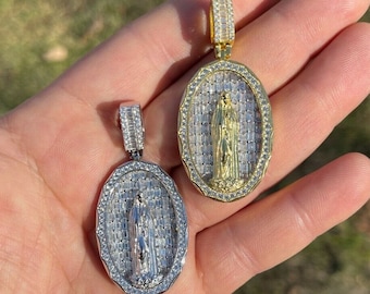 Puede incluir: Dos colgantes de forma ovalada con una figura religiosa en el centro. Ambos colgantes están rodeados de piedras transparentes en forma de baguette. Un colgante es de oro y el otro de plata.