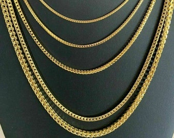 Könnte beinhalten: Ein Set aus fünf goldenen Kettenhalsketten in verschiedenen Breiten, auf einem schwarzen Samt-Hintergrund präsentiert. Die Ketten sind alle aus glänzendem, poliertem Metall und haben ein klassisches, schlichtes Design.