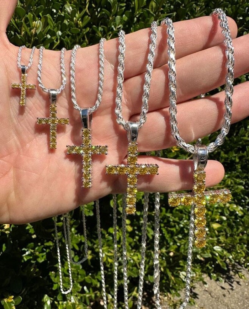 May include: Five silver rope chains with yellow diamond cross pendants. The chains are of varying lengths and the crosses are of different sizes.