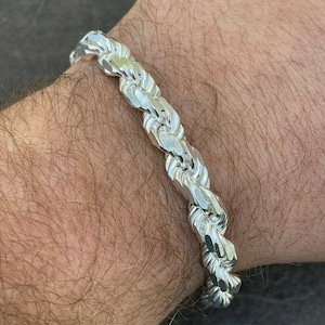 Puede incluir: Un brazalete de cadena de cuerda de plata con un dise&ntilde;o trenzado.