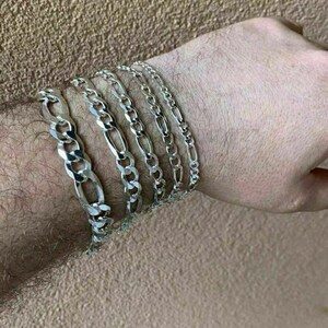 May include: A set of five silver chain bracelets, each with a different width and length, stacked on a person's wrist.