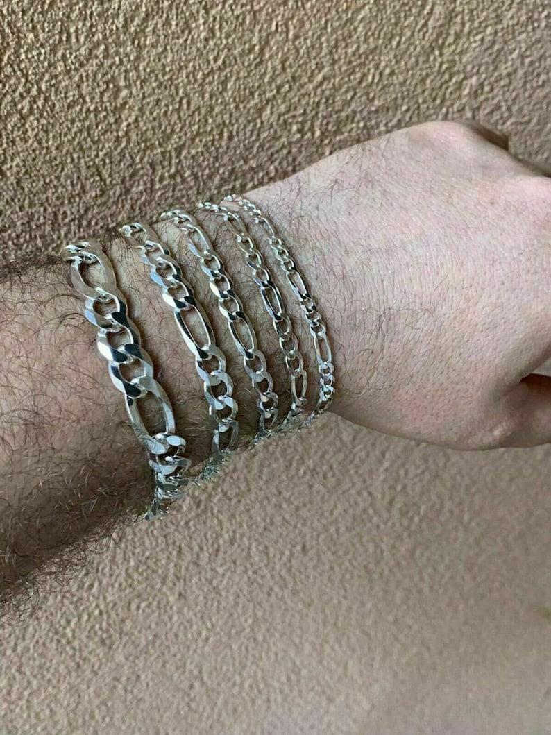 May include: A set of five silver chain bracelets, each with a different width and length, stacked on a person's wrist.
