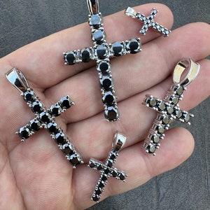 May include: Four silver cross pendants with black cubic zirconia stones. The crosses are of different sizes.