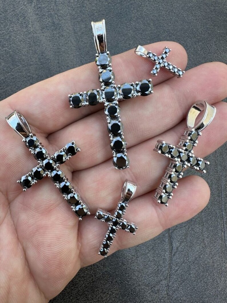 May include: Four silver cross pendants with black cubic zirconia stones. The crosses are of different sizes.