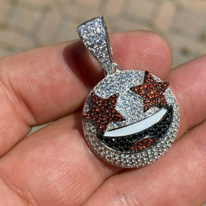 Puede incluir: Colgante de plata con un dise&ntilde;o de cara sonriente. La cara sonriente tiene ojos de estrella roja y una boca en blanco y negro. El colgante est&aacute; cubierto de piedras de circonita c&uacute;bica transparentes y rojas.