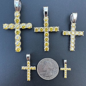 May include: Four silver cross pendants with yellow cubic zirconia stones. The pendants are arranged in order of size, with the largest pendant at the top and the smallest pendant at the bottom. A US quarter is included for size reference.