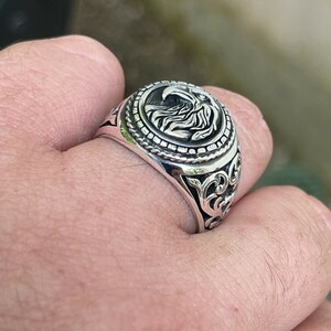Puede incluir: Un anillo de plata con un dise&ntilde;o de &aacute;guila en la parte superior. El anillo tiene detalles intrincados y un acabado texturizado.