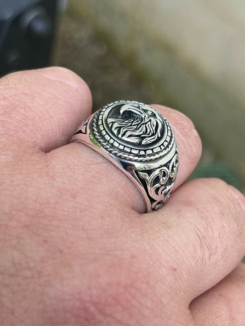 Puede incluir: Un anillo de plata con un dise&ntilde;o de &aacute;guila en la parte superior. El anillo tiene detalles intrincados y un acabado texturizado.